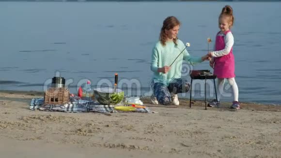 母女俩在沙滩上的烧烤上煎棉花糖和蔬菜视频的预览图
