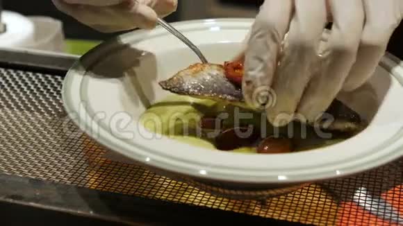 男人手里拿着乳胶手套把煮熟的鱼放在盘子里配上蔬菜和白酱厨师视频的预览图