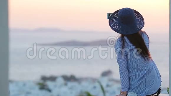 年轻的女人正在看一个著名的村庄Mykonos的大海上的日落背景是古老的建筑软软软视频的预览图