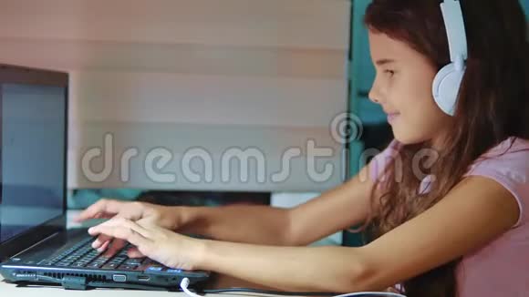 小女孩带着耳机在笔记本电脑上玩网络游戏电脑上的小女孩在社交中写了一条信息视频的预览图