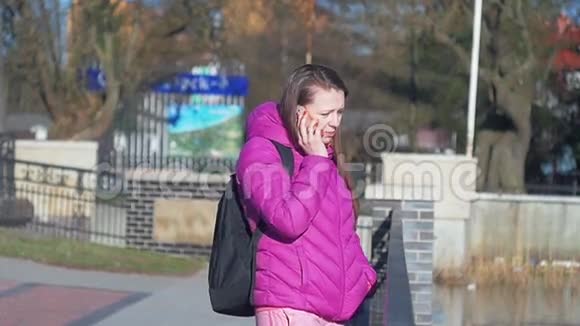 美丽的少女在公园在湖边打电话粉色衣服春装慢镜头中镜头视频的预览图