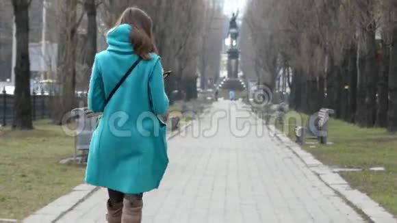 穿着蓝色外套的小女孩在公园里散步接电话视频的预览图