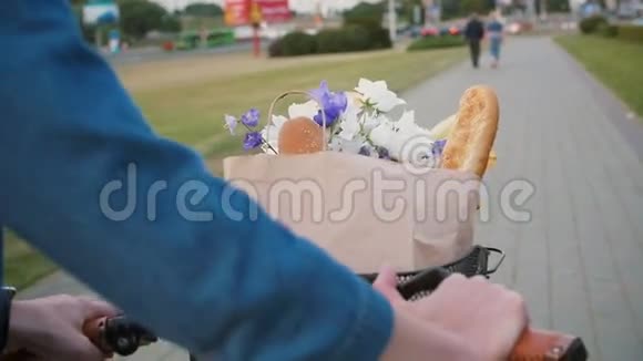 当她走在街上的时候女人手里拿着自行车的把手篮子里放着鲜花和面包慢悠悠的稳健的镜头视频的预览图