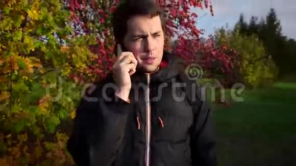 穿着黑色夹克的年轻人在秋天公园慢动作中打电话视频的预览图
