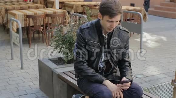 年轻人在街凳上用智能手机发短信年轻的高加索人用智能手机从互联网上购买商品视频的预览图