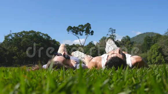 年轻夫妇躺在公园的绿草上放松男人和女人坐在草地上女孩和男孩视频的预览图