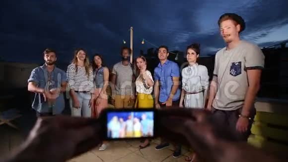 双手捧着电话拍摄一群向镜头挥手的快乐朋友视频的预览图