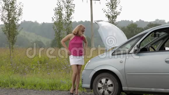 一个金发女孩在乡间小路上的一辆敞篷汽车旁惊慌失措地打着手机视频的预览图