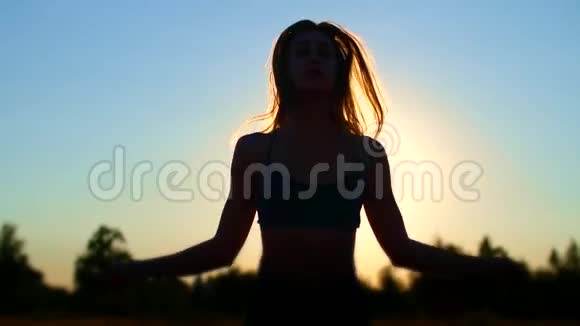 一个美丽的运动的金发碧眼的女孩的轮廓在夕阳下在蓝天的映衬下跳绳视频的预览图