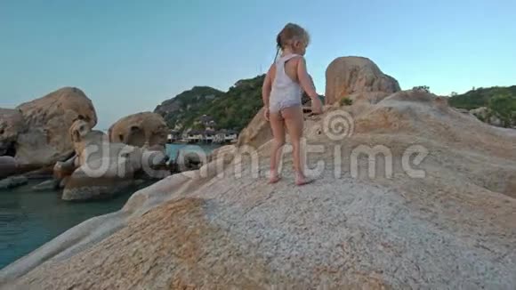 小女孩站在海滩日落的大裸岩顶上视频的预览图