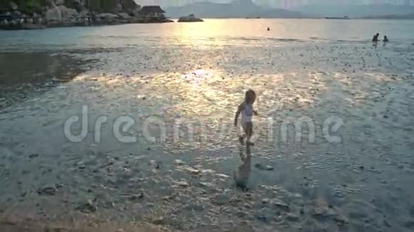 日落时分小女孩在海水中与海滩嬉戏视频的预览图