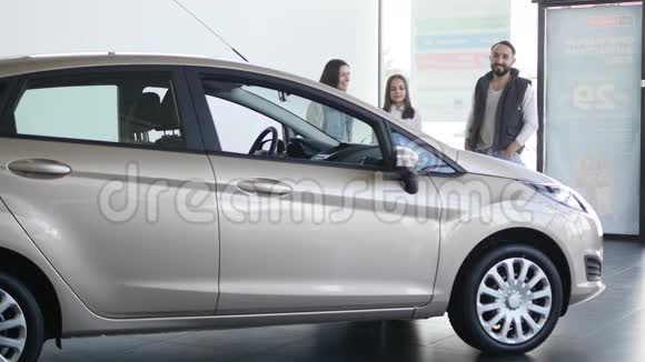 年轻的一家人停在经销商的灰色汽车附近坐在车里视频的预览图