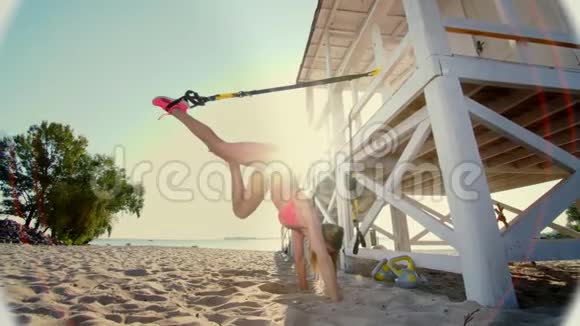 运动员穿着泳衣的年轻女子站在她的手上倒着用健身TRX系统做运动TRX视频的预览图