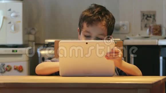可爱的小孩手里拿着一台白色平板电脑在家里的一张桌子上休闲服装视频的预览图