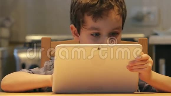 波特瑞特一个可爱的小孩手里拿着一台白色平板电脑在家里的一张桌子上休闲服装视频的预览图