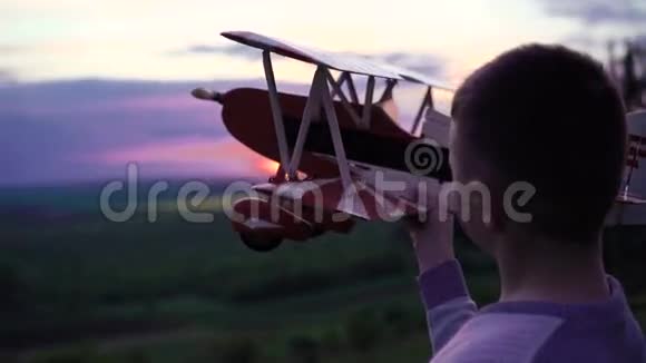 男孩抱着自制的飞机在日落背景的岩石上4k视频的预览图