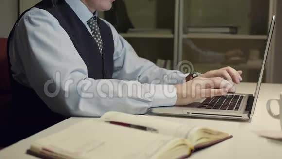 穿着西装戴着领带在办公桌前用笔记本电脑打字的英俊黑发男子视频的预览图
