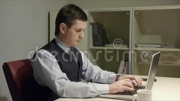 穿着西装戴着领带在办公桌前用笔记本电脑打字的英俊黑发男子视频的预览图