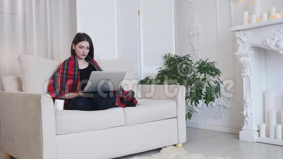 年轻女子坐在客厅的沙发上用手提电脑喝咖啡视频的预览图