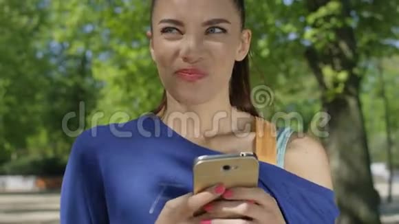 阳光公园里一个微笑的美丽女人在手机上发短信的肖像视频的预览图