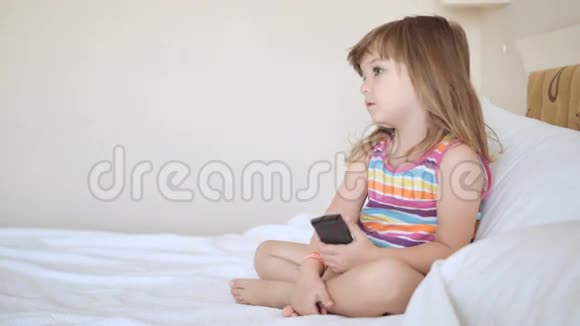 可爱的孩子穿着五颜六色的衣服在床上看电视视频的预览图