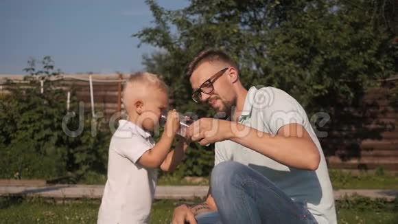 爸爸在花园里给他的儿子喝水小男孩饮水视频的预览图