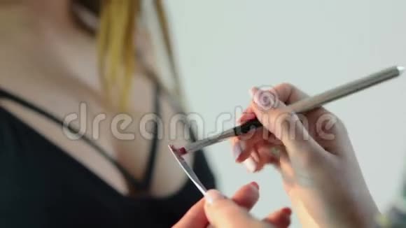 化妆师在一个年轻漂亮女人的嘴唇上用刷子涂红色口红视频的预览图