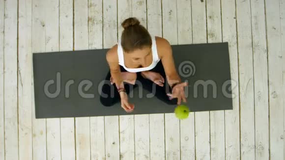 漂亮的女人拿着绿苹果带着它的丛林坐在运动垫上视频的预览图