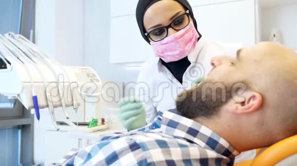 戴头巾的女性牙医在病人牙齿上拍摄视频的预览图