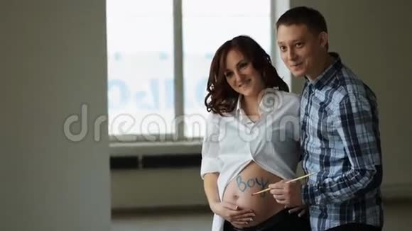 一位年轻有创造力的丈夫在男孩这个词的腹部写下了蓝色的油漆站在幸福怀孕的妻子旁边视频的预览图