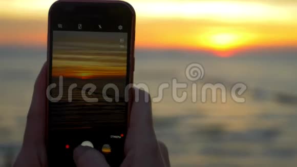 一个带着手机的女人在日落时拍了一张热带海滩的照片视频的预览图