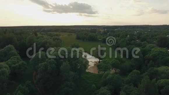 俄罗斯夏季日落时在蓝天太阳和云彩的映衬下森林湖泊和乡村房屋的景色视频的预览图