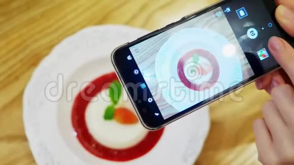 特写镜头女性的双手在一家餐馆的智能手机上拍下潘纳卡塔甜点的照片视频的预览图
