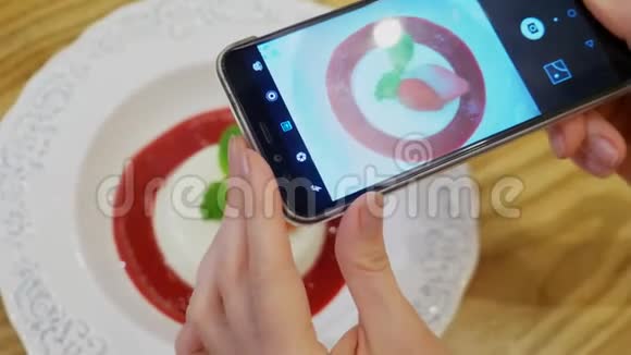 特写镜头女性的双手在一家餐馆的智能手机上拍下潘纳卡塔甜点的照片视频的预览图