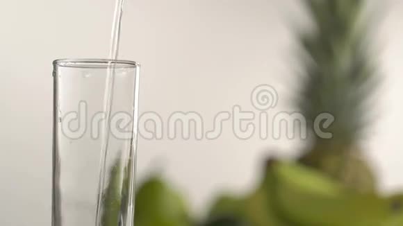 在绿苹果菠萝和玻璃模糊的背景下水涌入高玻璃的特写镜头视频的预览图