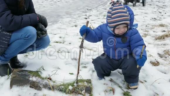 可爱的宝宝在冬天在街上和妈妈玩在树枝上的男孩视频的预览图