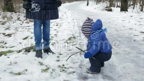 可爱的宝宝在冬天在街上和妈妈玩在树枝上的男孩视频的预览图