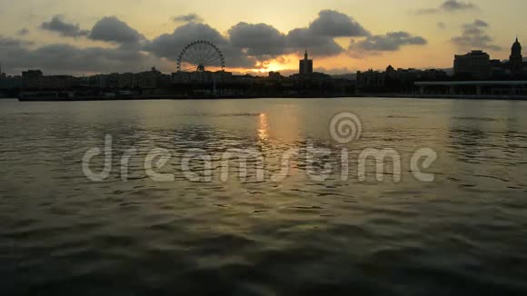 日落时分马拉加城的摩天轮旋转和天际线平静的大海视频的预览图