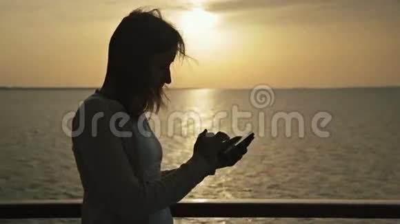 日出游轮甲板上带智能手机的女性剪影视频的预览图