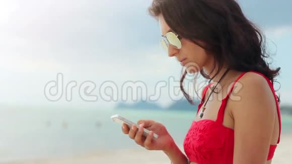 迷人的年轻女子在海滩上用手机视频的预览图