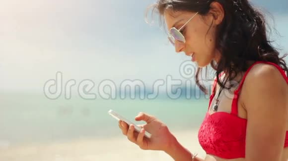 迷人的年轻女子在海滩上用手机视频的预览图
