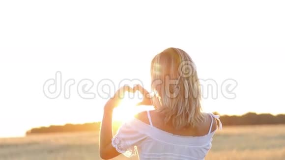 美丽的女孩用她的双手在大自然日落的背景下做着心视频的预览图