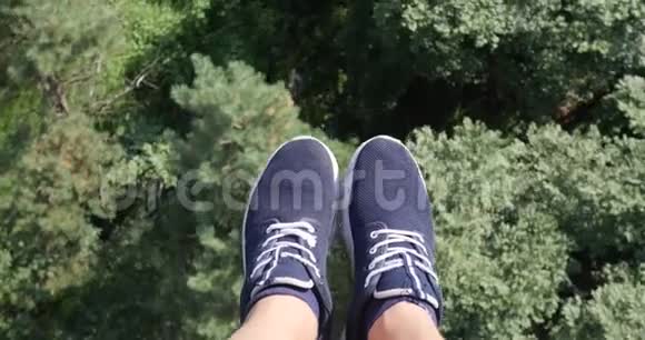 空中POV视图飞过美丽的森林树木空中相机拍摄和人的腿与蓝色运动鞋的框架视频的预览图