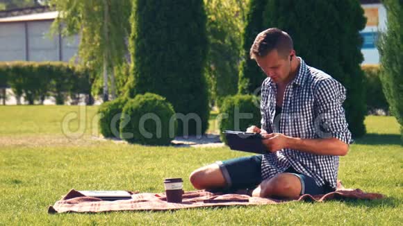 在公园里坐在毯子上的年轻人用笔记本电脑视频的预览图