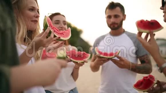 快乐的朋友吃西瓜站在沙滩上聊天穿蓝色牛仔裤的年轻男女视频的预览图