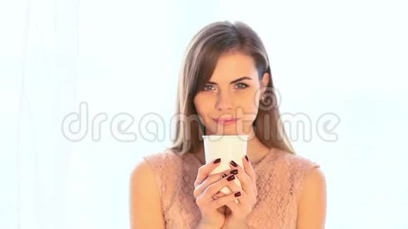 女孩站在窗前喝热茶或咖啡视频的预览图