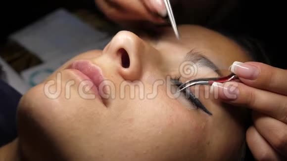 长睫毛的女人眼睫毛延伸用镊子粘合人造睫毛一个女人躺在灯下视频的预览图
