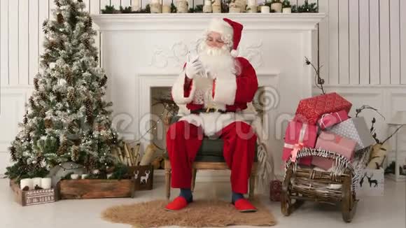 圣诞老人快乐地在电话里念圣诞信息坐在椅子上微笑视频的预览图