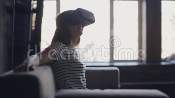 年轻女子坐在客厅的沙发上使用VR耳机视频的预览图