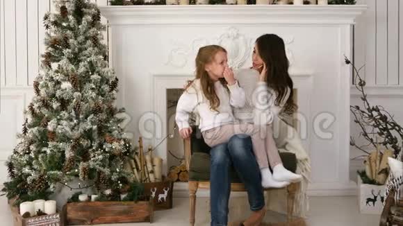 年轻的母亲在打电话女儿坐在圣诞树旁边的膝上有点无聊视频的预览图